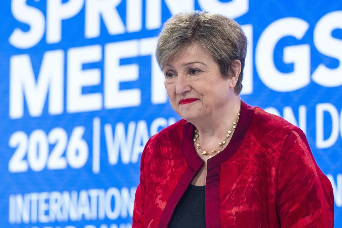 Woman in a red velvet jacket and pearl necklace smiling at a conference with a blue backdrop that reads 'Spring Meetings 2026'.