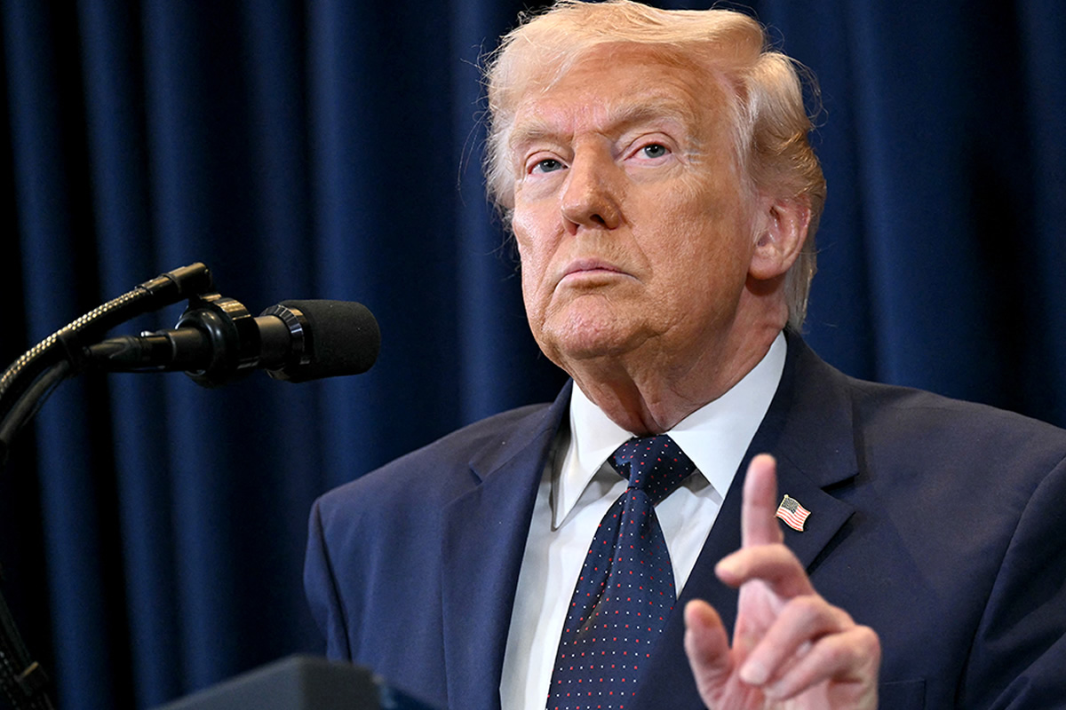 Former U.S. president Donald Trump speaking at a podium with a microphone, wearing a dark suit and tie.