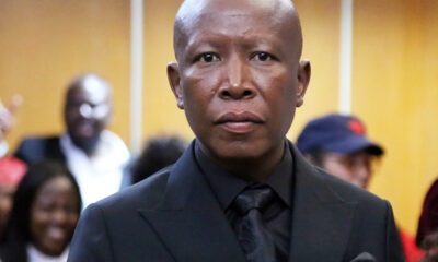 Close-up of an African man in a black suit and tie at a formal event, with a blurred crowd in the background