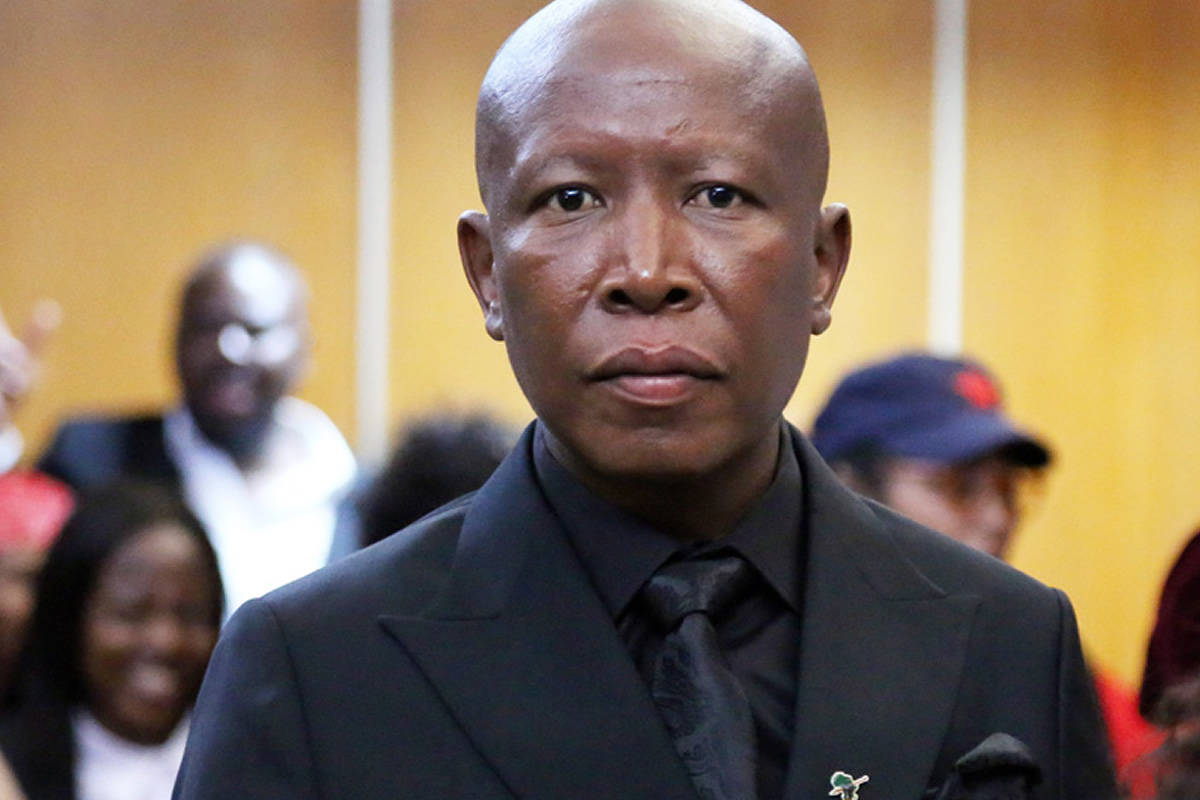 Close-up of an African man in a black suit and tie at a formal event, with a blurred crowd in the background