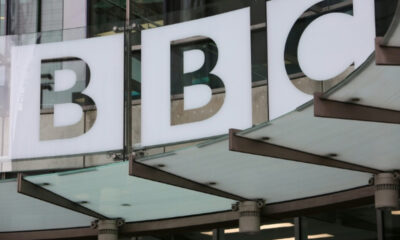 Front of a building with large white signs displaying the letters BBC on glass panels.
