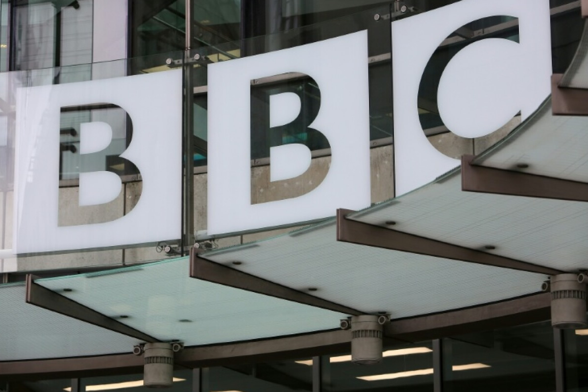 Front of a building with large white signs displaying the letters BBC on glass panels.